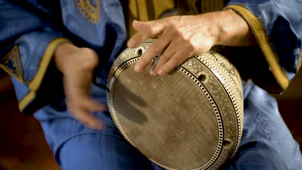 Tight shot of man in Moroccan dress playing arabic doumbek, darbuka, or derbeki alt