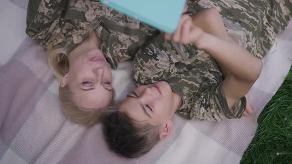 High Angle View Joyful Military Woman and Teenage Boy Surfing Internet on Tablet Talking Laughing in alt