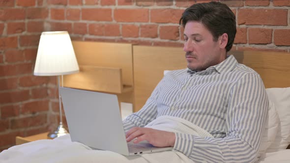Middle Aged Man Working on Laptop in Bed alt