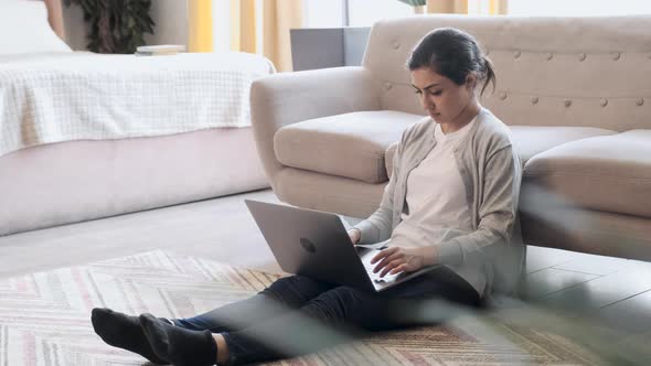 Young woman sitting on floor at home working with laptop and documents alt