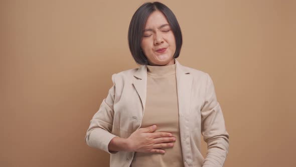 Asian business woman was sick with stomach ache and standing isolated over beige background.