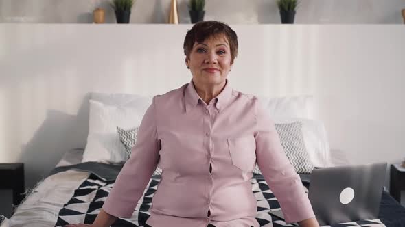 Mature Woman Looking at Camera and Sitting at Bed alt