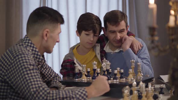 Portrait of Happy Caucasian Grandfather and Grandson Playing Chess with Boy's Young Father alt