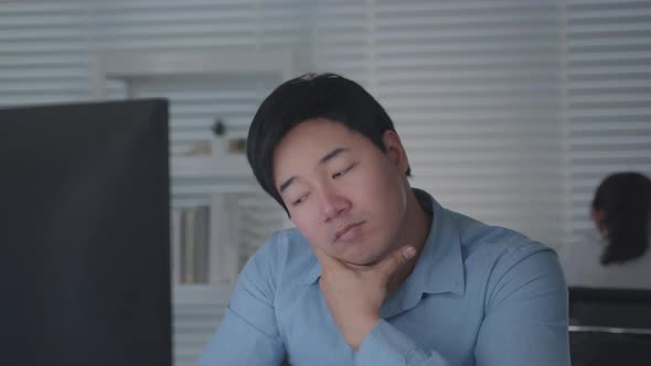 Tired Asian Male Worker Working on desktop computer in the Corporate Office,