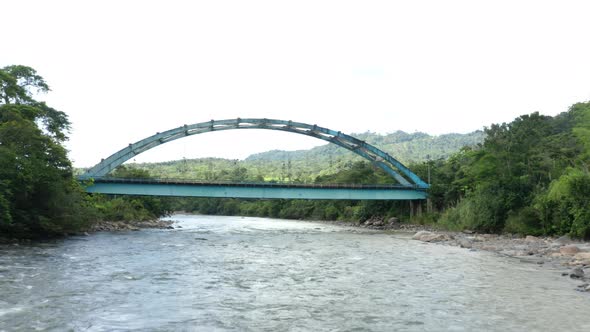 Aerial view over a broad river with a metal truss bridge, passing the bridge alt