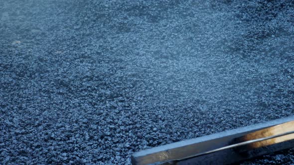 Worker Operating Asphalt Rake During Road Construction