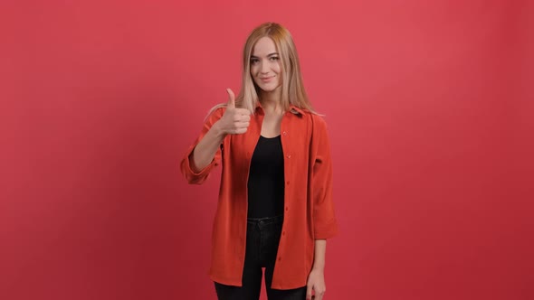 Portrait of Attractive Young Woman Showing a Thumbs Up on Red Background alt