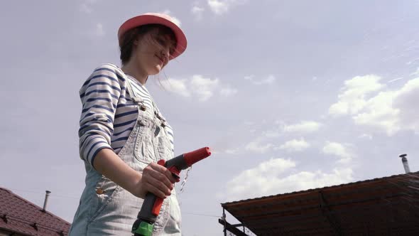 Young Smiling Girl Watering Garden From Garden Hose on Hot Summer Day alt