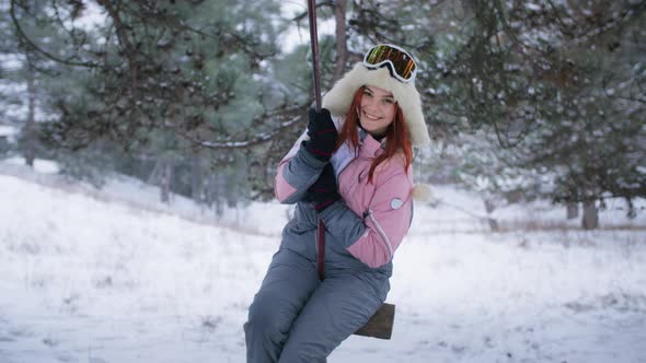 Active Leisure Portrait of Smiling Happy Woman in Hat and Ski Goggles Having Fun Riding on Swing
