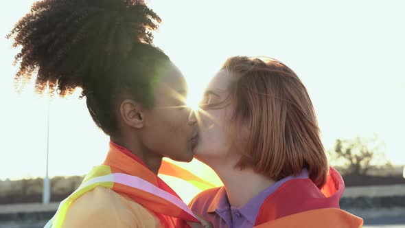 Mulitracial lesbian girls kissing together at gay pride parade while holding rainbow flag - LGBT