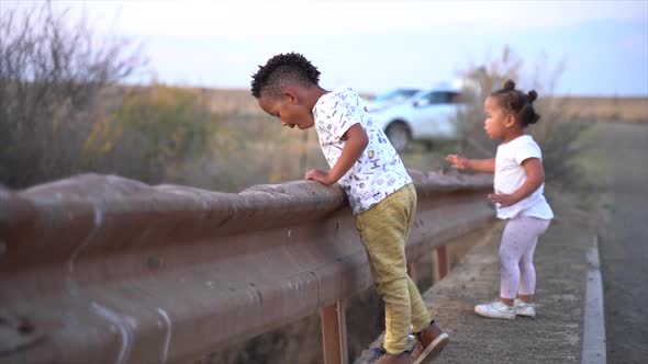 South African boy and girl on a low bridge in a winter country landscape at dusk alt