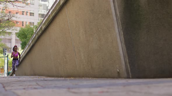 African american woman wearing earphones running in the sidewalk alt