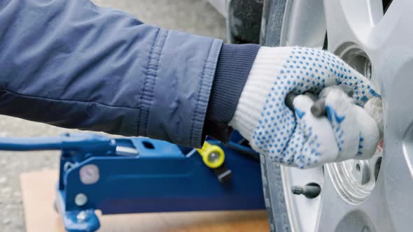 Hands of Mechanic Unscrewing Car Wheel Bolts and Holding Them alt