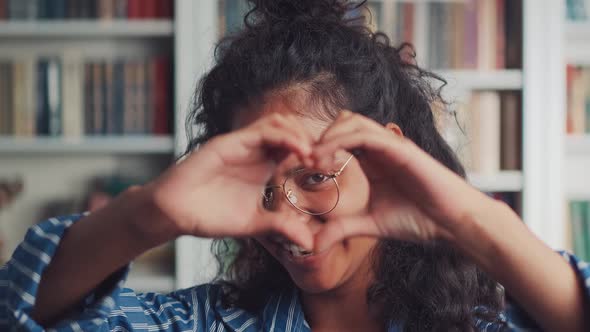 Smiling Young Indian Woman Showing Hands Sign Heart Shape Looking at Camera alt