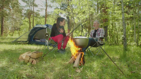 Cheerful Backpackers Talking and Relaxing Near Campfire During Hike alt