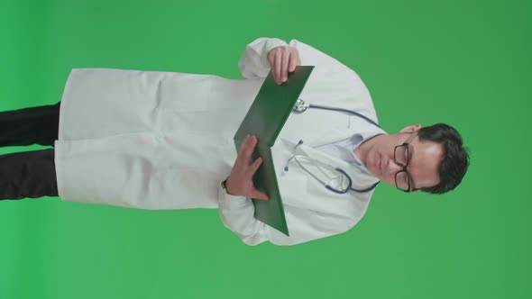 Asian Doctor With Stethoscope opening Document File And Reading While Walking On Green Screen alt