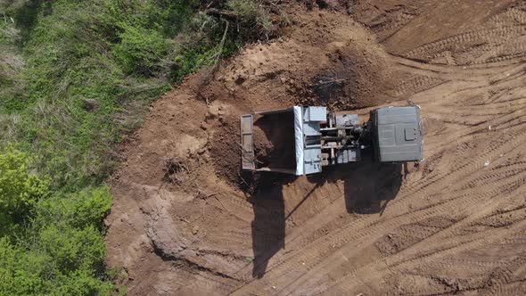 Top aerial view of tipper unloading ground on further construction site