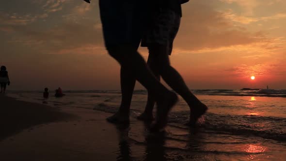 Older Couple Holds Hands and Walks Down the Beach at Sunset Getting Their Feet Wet