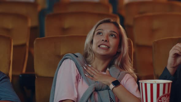 Attractive cheerful young caucasian woman watching horror movie in cinema theate. alt