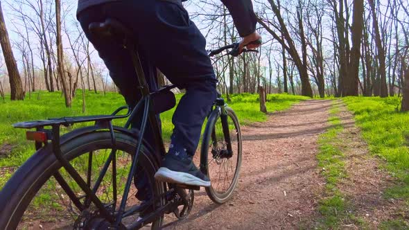 Young Guy Rides a Bicycle Along a Path in a Green Forest Rear View in Slow Mo alt