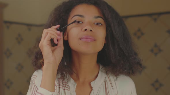 Close Up of 20s African American Woman Applying Mascara Looking at Camera in Bathroom alt