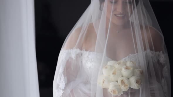 Bride in White Dress Staying Near Window with Flowers Bouquet Wedding Morning Preparations at Home alt
