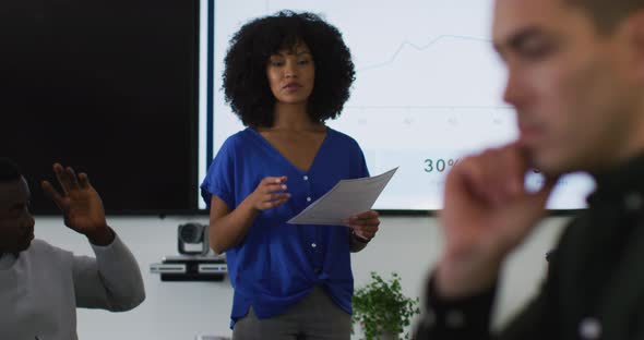 Mixed race businesswoman giving presentation to diverse group of colleagues in meeting room alt