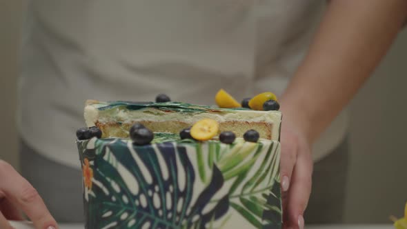 Holding Half of Cake Decorated with Mango Passion Fruit and Blueberry in Slow Motion alt