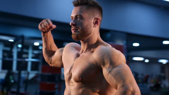 Circle view on bodybuilder without shirt in gym. Man with strong hands and big muscles. alt