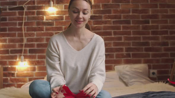 Caucasian Woman is Packing Gift While Sitting on Bed alt