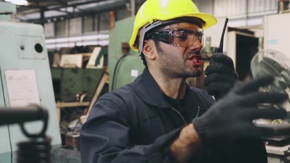 Factory Worker Talking on Portable Radio While Inspecting Machinery Parts alt