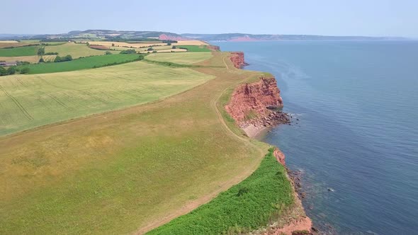 4K Aerial, flying slow over red cliffs by a UK coastal town during summer holiday alt