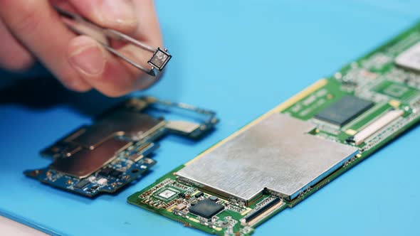 Worker Removing Broken Item From Circuit Board with Tweezers alt