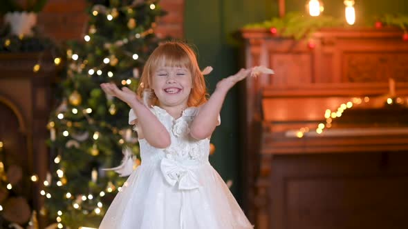 cute little girl in a white dress is playing in the room against the background of a Christmas tree