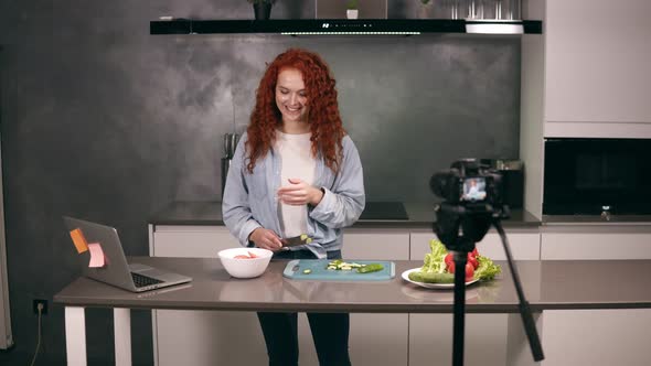 Young Woman in Casual Clothes Leads a Culinary Blog and Records Video in Grey Kitchen's Bar alt
