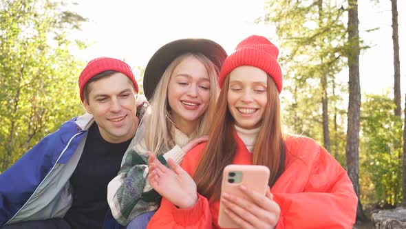 Three Caucasian Friends Rest on Mountains Use Smartphone