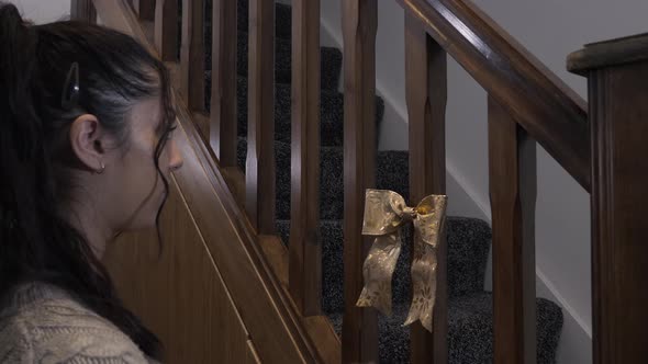 Teenage Female Sticking Double Christmas Bows With Gold Leaf Design On Stair Spindles. Locked Off alt