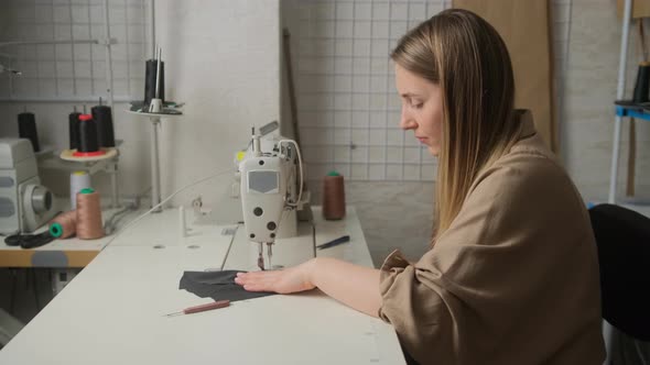 woman seamstress works at a sewing machine in workshop, enjoys the process. Fashion business alt