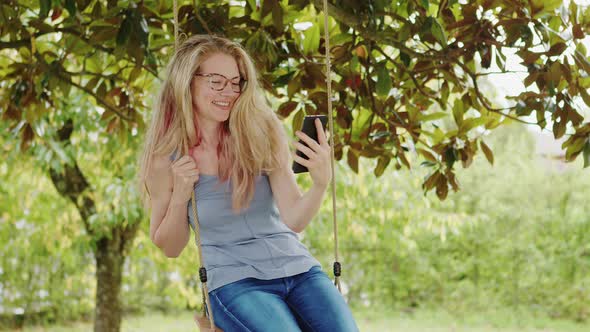 Smiling blonde woman with eyeglasses using smartphone