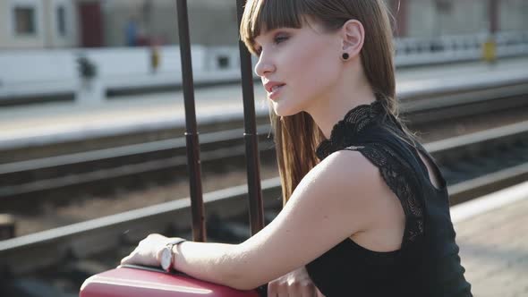 Portrait of Attractive Girl Looks Around on Railway Station and Smiles Gently alt