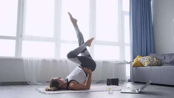 Young Woman in Top and Leggings Raises Legs in Yoga Asana