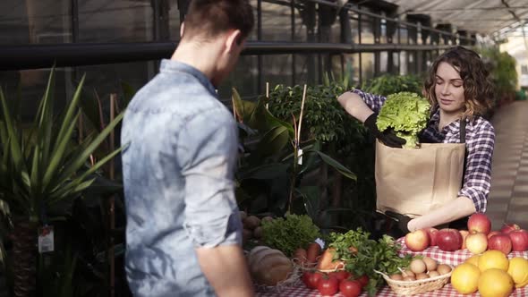 Brunette European Saleswoman Wearing Apron Helping with a Customer's Choice Putting a Pile of Green alt