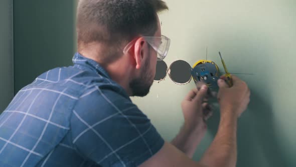 Electrician Repairs Plug on with Screwdriver in Light Room alt