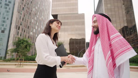Happy Muslim Arab Man Shaking Hands with Caucasian Female Partner During Meeting Outdoors alt