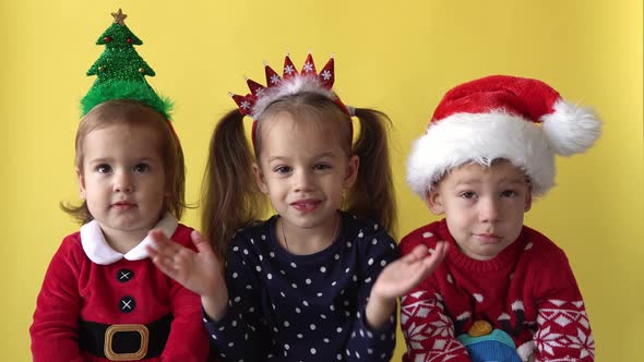 Emotion Cute Happy 3 Siblings Friends Baby Girl And Boy Applaud in Santa Suit Looking On Camera At