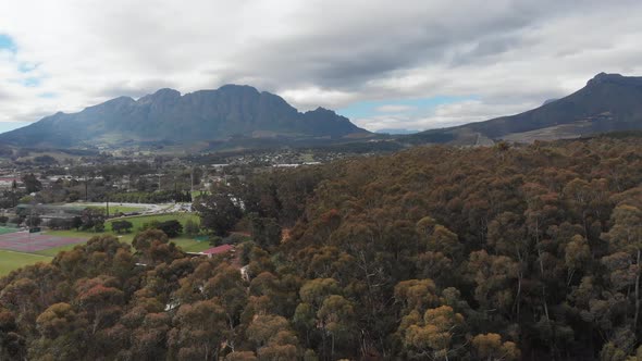A shot rising over woods reveals a town in front of a mountain. The shot was taken in Stellenbosch, alt