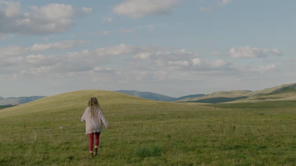 4k Rear view of Happy woman with dreadlocks Runs through a Field under sunlight in evening. alt