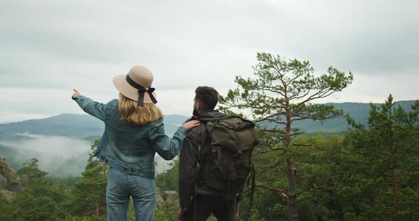 A Woman and a Man are Standing on Top of a Cliff and Looking at Nature alt