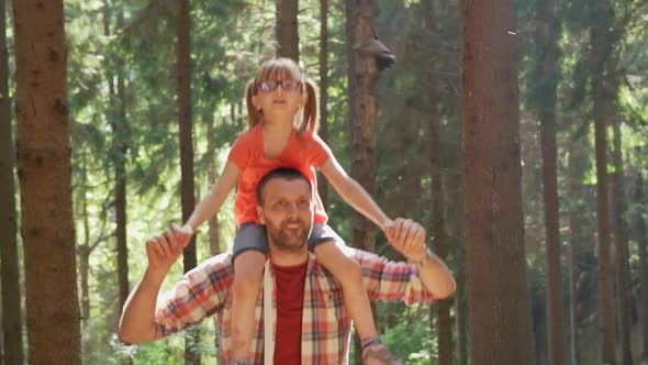 Front View of Father Giving a Piggyback Ride to Daughter Walking in Forest alt
