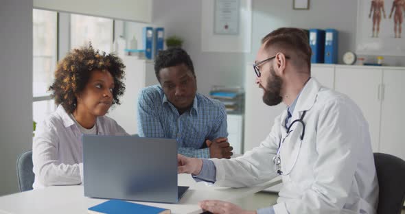 African Couple Looking at Ultrasound Baby Image on Screen of Laptop at Doctor Office alt